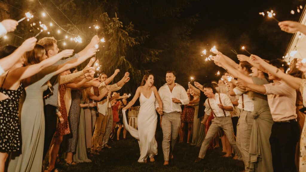 Bride and groom joyfully exit surrounded by sparkling celebratory guests at a nighttime wedding.