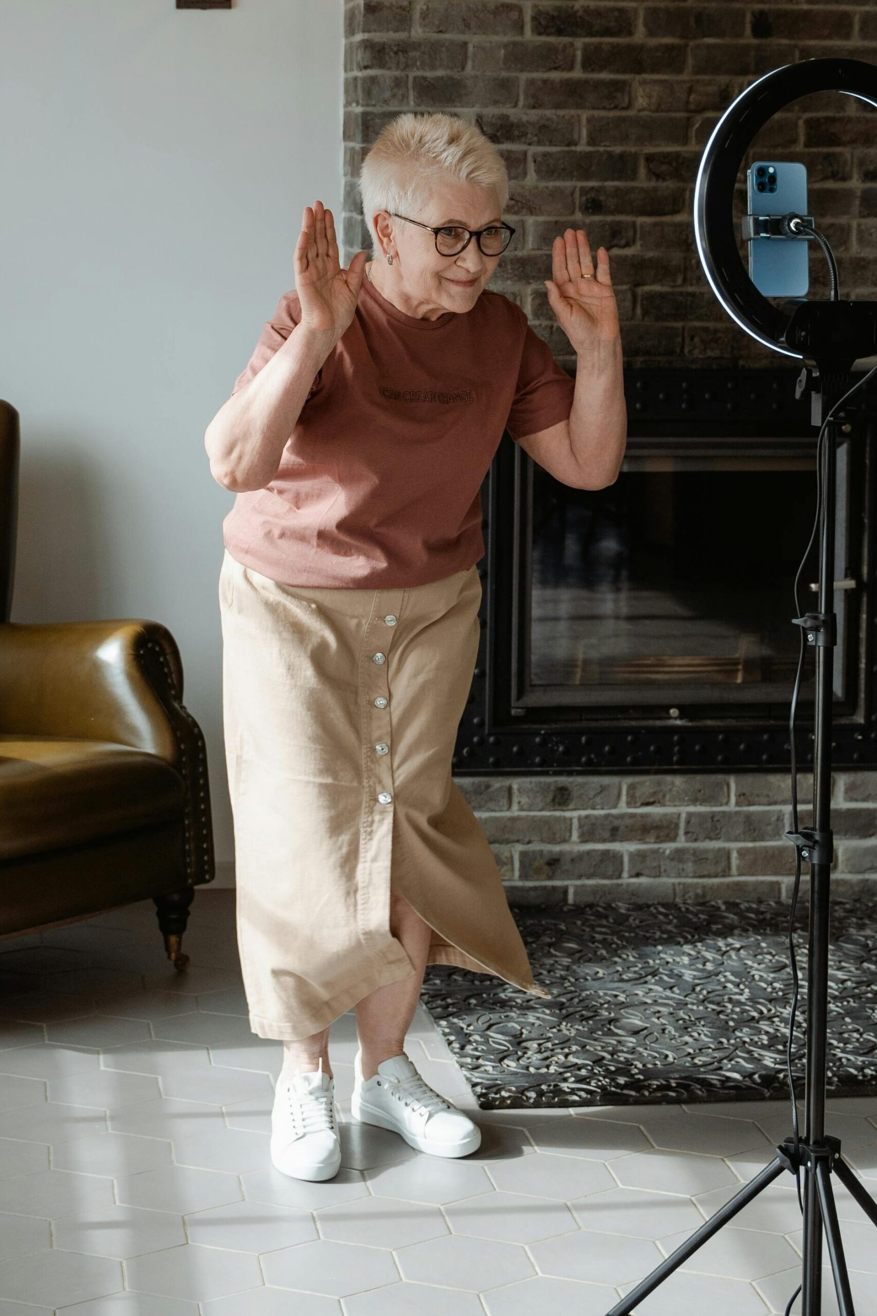 Joyful senior woman dancing indoors next to a camera setup in a cozy living room.